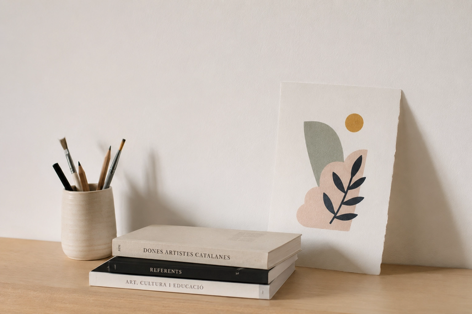 Materials artístics i llibres sobre dones artistes catalanes en un espai de treball minimalista.